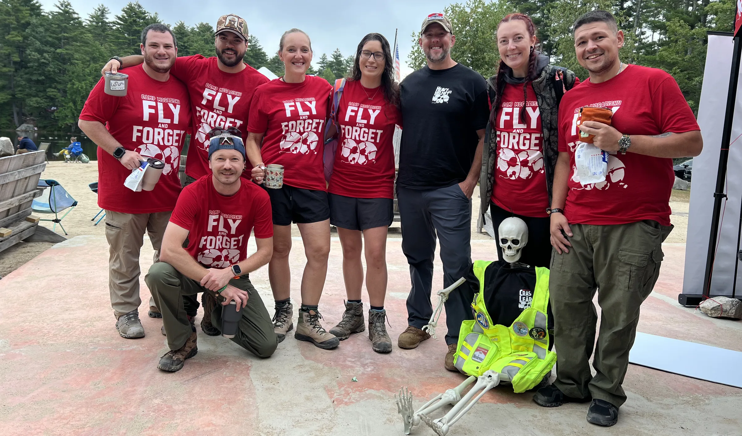 Residents of Camp Mogadishu in Fly and Forget shirts, with Cal seated in a high-visibility vest, at Acres of Wildlife Campground.